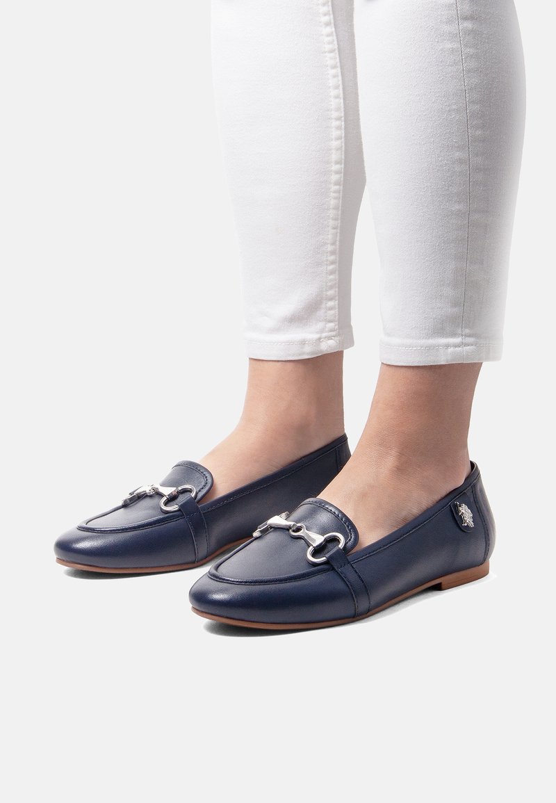 Marinblå lädersandaler med silverdetaljer, rund tå och en lågprofil-design. Matchas med vita avskurna jeans.