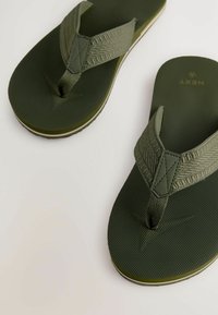 Infradito verdi con cinturini texturizzati e una soletta decorata. Suola leggermente rialzata con un accento bianco a contrasto lungo il bordo.
