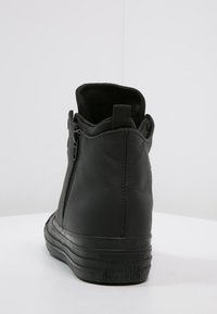Schwarze Leder-Hochschaft-Sneaker mit strukturierter Oberfläche, Reißverschluss und Gummisohle, die das "Converse All Star"-Logo an der Ferse trägt.