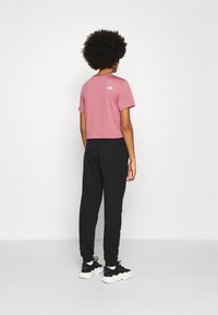 Camiseta cropped rosa de manga corta, con un pequeño logo en la parte posterior, combinada con joggers negros y zapatillas negras.