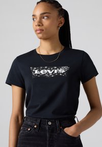 Black cotton t-shirt featuring a white Levi's logo in a distressed print. Short sleeves and a crew neckline with a relaxed fit.