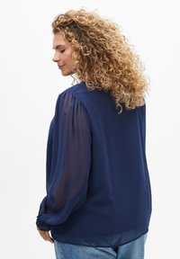 Blouse marine avec des manches longues transparents, des détails froncés aux épaules et aux poignets, une coupe fluide et un ourlet arrondi.