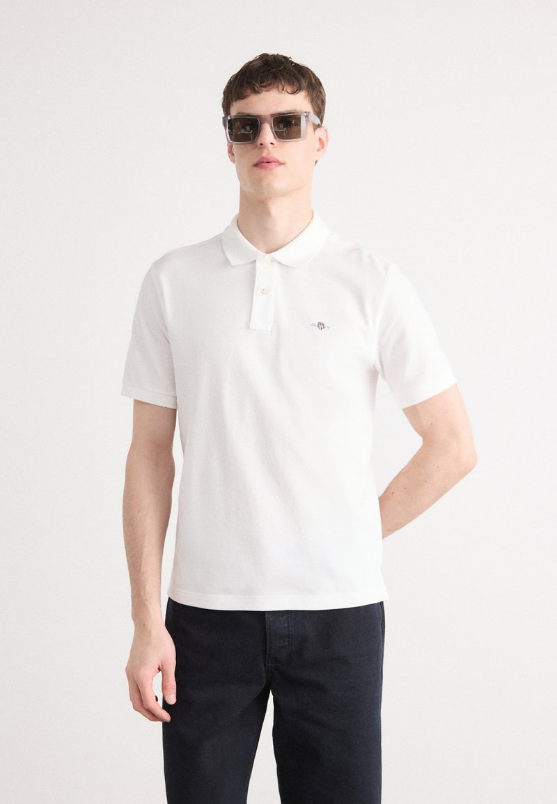 Hvit polo skjorte i myk stoff, med klassisk krave, to-knapps placket og en liten logo på brystet. Brukes med mørke denimjeans.