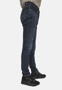 Jeans in denim blu slim, con vita media, dettagli sbiaditi e scarpe sportive nere. Presentano un design a cinque tasche e accenti di cucitura.
