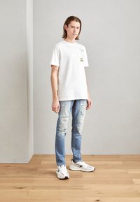 Camiseta de algodón blanca con un estampado gráfico, combinada con unos jeans de mezclilla desgastados de color azul claro y zapatillas blancas con acentos negros.