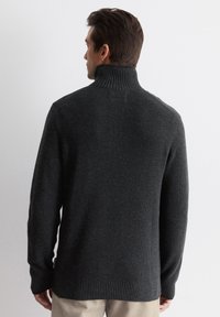 Dark gray knit sweater with a high ribbed collar, long sleeves, and a slightly loose fit, featuring a textured surface and ribbed hem.