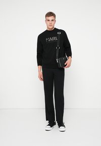 Svart sweatshirt med "KARL LAGERFELD" logotyp, matchad med svarta byxor och svarta sneakers. Liten axelväska med justerbar rem.