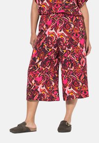 Multikleurige cropped broek in een abstract patroon van roze, rood en zwart, met een elastische taille en gecombineerd met bruin instapschoenen.