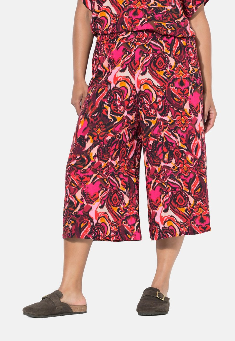 Multikleurige cropped broek in een abstract patroon van roze, rood en zwart, met een elastische taille en gecombineerd met bruin instapschoenen.