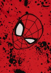 Maschera di Spiderman con motivo a ragnatela e occhi bianchi su uno sfondo di tessuto rosso con schizzi di vernice nera.