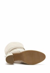 Stivale beige con design sblusato, materiale scamosciato morbido e suola in gomma con scanalature testurizzate, visto dal basso.