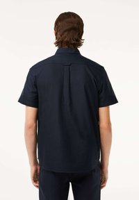 Camicia navy a maniche corte con colletto classico, piega sul retro per facilitare i movimenti e un tessuto liscio e strutturato.