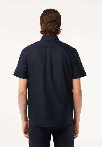 Chemise à manches courtes bleu marine avec un col classique, un pli dans le dos pour faciliter le mouvement et un tissu lisse et texturé.