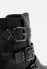 Zwarte leren enkelboot met meerdere verstelbare banden, zilveren gespen en studdetails. Glad textuur met zichtbare stiksels.