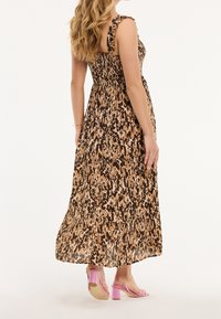 Vestido largo con un estampado abstracto en tonos marrón, beige y negro, con tirantes con volantes y una silueta fluida. Combinado con sandalias de tacón ancho rosa.