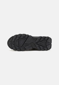 Semelle extérieure de chaussure de sport noire avec un motif de traction profond et multidirectionnel ; matériau durable avec une finition texturée et des accents triangulaires.