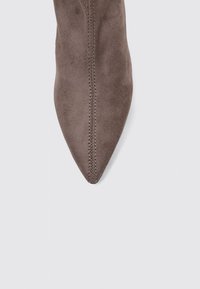 Bottine en daim marron avec un bout pointu et des coutures visibles le long du centre. Texture lisse et design minimaliste.