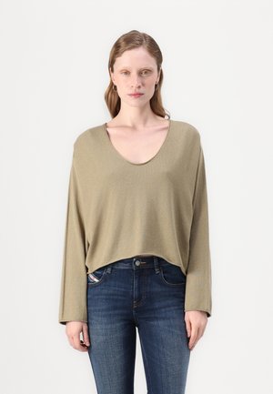 Oliven grønn løs langermet topp med bred V-hals, myk tekstur og cropped hem, parret med mørke denimjeans.