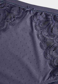 Donkerpaarse lingerie met delicate kantafwerkingen met bloemmotieven, een stippenstructuur en een klein strikje aan de bovenkant.