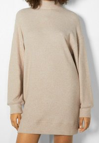 Robe pull beige côtelée avec un col montant et des manches longues, présentant une coupe décontractée et une texture douce, arrivant à mi-cuisse.