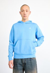Haut à capuche bleu clair avec une poche avant, un cordon de serrage pour la capuche et un logo Jumpman blanc sur la poitrine. Texture de tissu lisse.