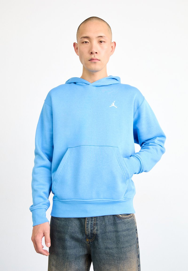 Haut à capuche bleu clair avec une poche avant, un cordon de serrage pour la capuche et un logo Jumpman blanc sur la poitrine. Texture de tissu lisse.