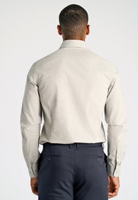 Helles graues Langarmshirt mit einer dezenten Textur und geknöpften Manschetten, kombiniert mit dunklen Marinehosen mit Seitentaschen und Knöpfen.