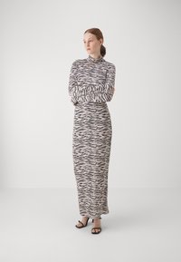 Langsleeve, jurkje met zebra-print in crème en zwart. Strak lijfje met plooidetail bij de taille. Gladde textuur, lange jurk.