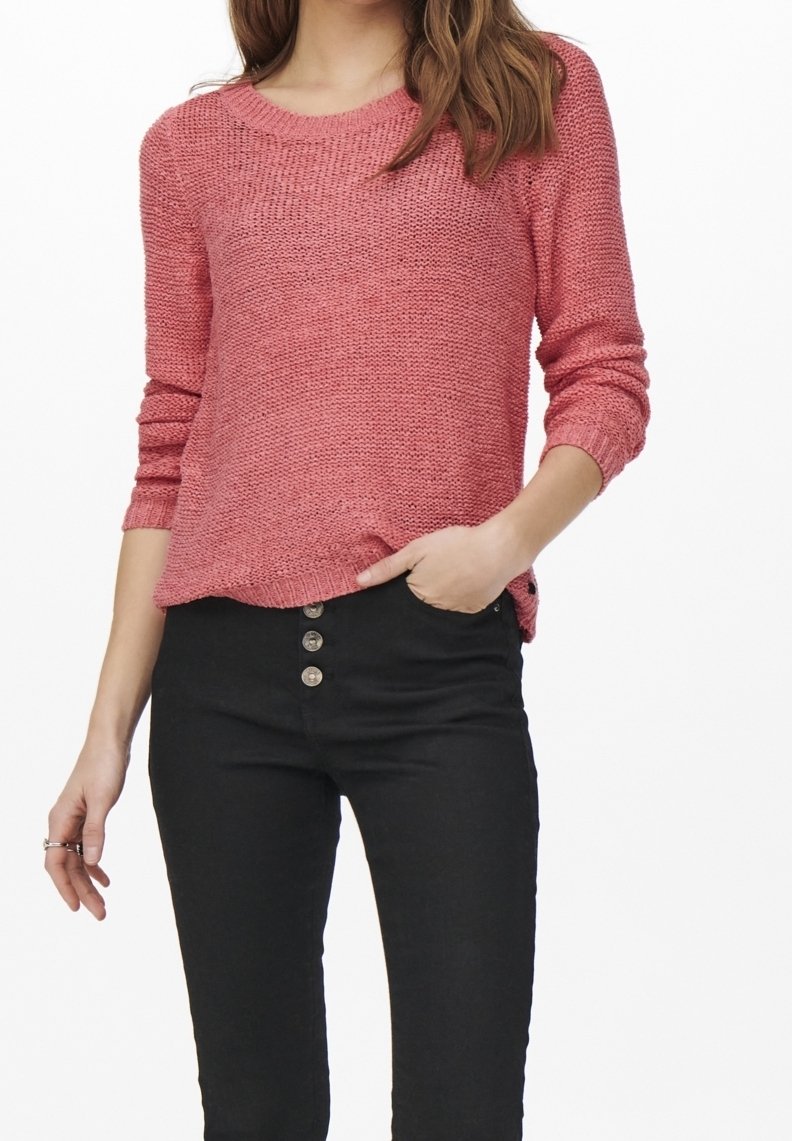 Pull en tricot rose avec un col rond et des poignets côtelés, associé à un jean noir taille haute avec cinq boutons métalliques.