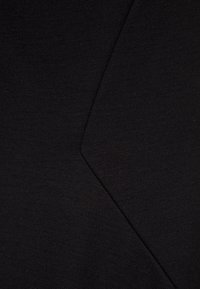 Tissu noir présentant un tissage texturé, avec un détail de couture en zigzag qui crée un intérêt visuel grâce à des formes et des lignes variées.