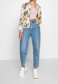 Chaqueta bomber floral con fondo rosa, hojas verdes y burdeos. Combinada con jeans de tiro alto azul y zapatillas blancas.