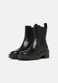 Bottes Chelsea en cuir noir avec semelles à crampons épaisses, panneaux élastiques latéraux et languettes à l'arrière pour faciliter l'enfilage.