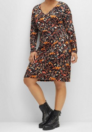 Schwarzes Langarmkleid mit floralem Muster in Orange- und Blautönen, V-Ausschnitt und figurbetonter Silhouette, kombiniert mit schwarzen Knöchelstiefeln.