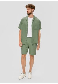 Lichtgroen, gestructureerd shirt met korte mouwen en een borstzak, gecombineerd met bijpassende korte broek. Wit t-shirt eronder. Draag het met witte sneakers.