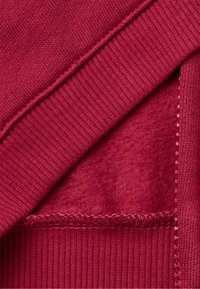 Czerwony sweter z dzianiny, z prążkowanymi ściągaczami, miękką podszewką i szwami typu flatlock. Teksturowana powierzchnia w połączeniu z gładkim, puszystym wnętrzem.