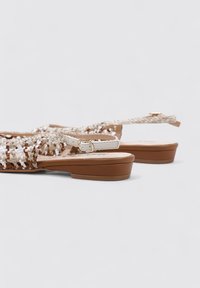 Sandalias trenzadas con una combinación de colores beige y marrón, con un upper texturizado, banda ajustable y una suela plana marrón para mayor comodidad.