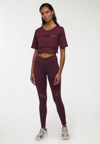 Burgundowy zestaw odzieży sportowej składający się z krótkiego topu z siateczkowymi wstawkami oraz legginsów o wysokim stanie z wycięciami. Gładki materiał o dopasowanym kroju.