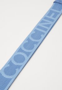 Cintura tessuta azzurro chiaro con motivo logo ripetuto, caratterizzata da una consistenza morbida e una forma rettangolare elegante per un aspetto moderno.