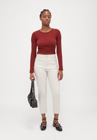 Red long-sleeve crop top, cream high-waisted pants, black strap heels, and a dark shoulder bag. Plain background.