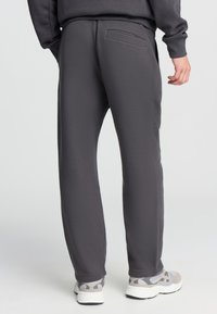 Szare dresy wykonane z miękkiego materiału, z tylną kieszenią i luźnym krojem, w połączeniu z jasnoszarymi butami sportowymi.