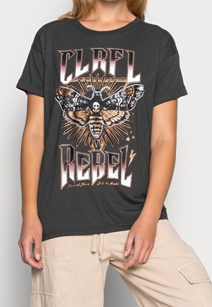 Persona che indossa una t-shirt nera con una grande grafica di una falena che mostra un teschio e le parole "CLRFIL REBEL" in lettere grassetto.