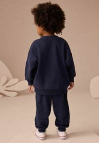 Granatowa bluza i pasujące dresy wykonane z miękkiego materiału. Charakteryzują się luźnym krojem, ściągaczami oraz prostymi białymi adidasami.