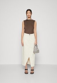 Braunes ärmelloses Oberteil, weißer Jeansrock mit einem Schlitz vorne, schwarze Plateausandalen und eine silberne strukturierte Tasche. Einfaches, modernes Design.