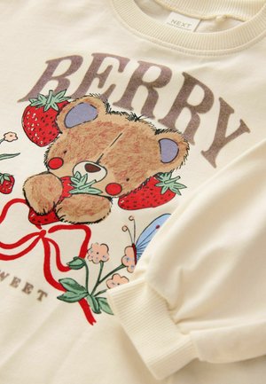 Kreemivärvi sweatshirt, millel on karu, kes hoiab maasikaid, ümbritsetud lillede ja liblikaga. Tekst ütleb "BERRY SWEET". Koonusmad varrukad.