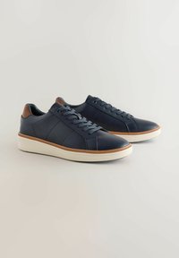 Sneaker in pelle blu navy con lacci azzurri, suola in gomma bianca testurizzata e dettagli in pelle marrone sul tallone. Design snello e cuciture.