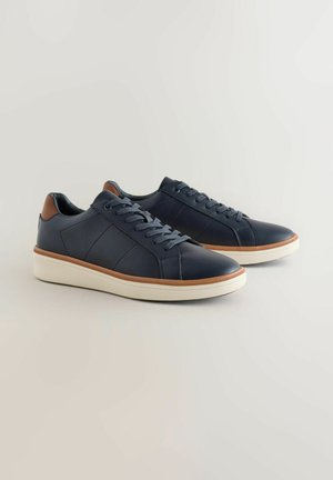 Granatowe skórzane sneakersy z jasnoniebieskimi sznurowadłami, teksturowaną białą gumową podeszwą i brązowymi skórzanymi akcentami na pięcie. Smukły design i przeszycia.