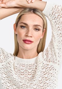 Maglione bianco lavorato a maglia con un design a motivi; presenta un collo rotondo e maniche voluminose. La modella ha i capelli biondi lisci e un trucco neutro.