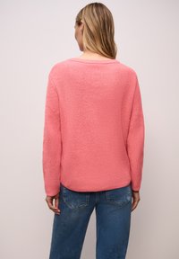 Pull en tricot rose à coupe ample et col rond. Tissu texturé avec un motif côtelé, associé à un jean en denim bleu.