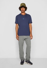 Marineblå bomulds t-shirt med korte ærmer og et firkantet logo, parret med lysegrå sweatpants og sorte sneakers med cremefarvede accenter. Olivengrøn kasket.