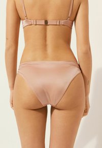 Světlý růžový bikini set s saténovým leskem. Nastavitelné ramínka a zapínání na zádech. Klasické spodní díly s jemnou, hladkou texturou.